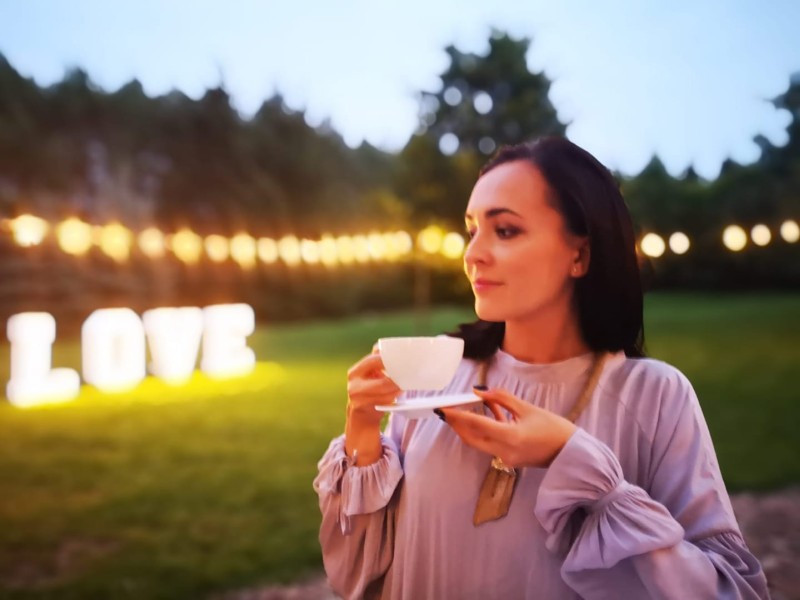 Aleksandra Płocka - zdjęcie profilowe. Aleksandra rozkoszuje się filiżanką kawy, w tle napis świecący ciepłym światłem